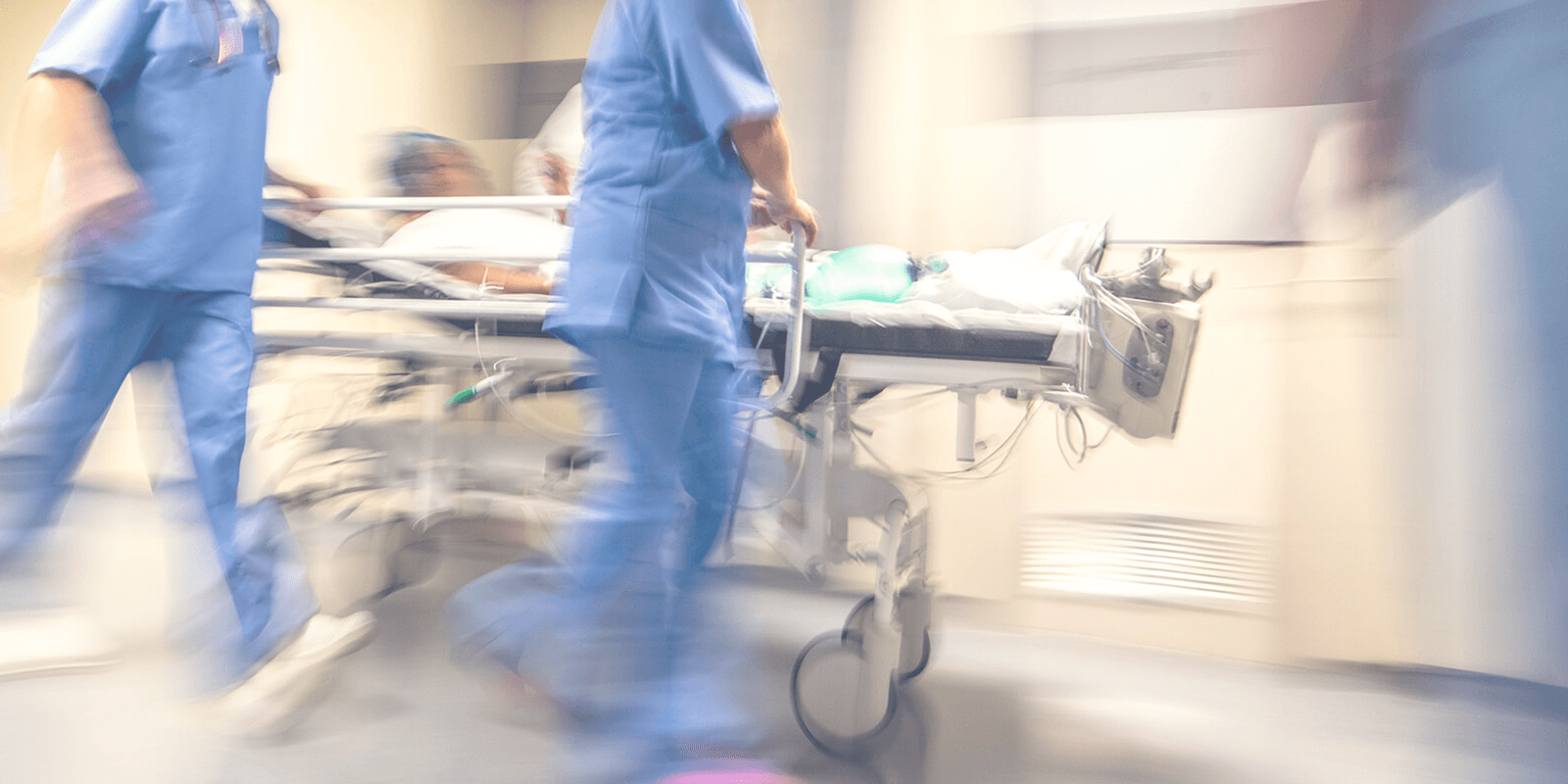 Nurses and hospital professionals in blue scrubs rolling a patient in a hospital bed down a hallway